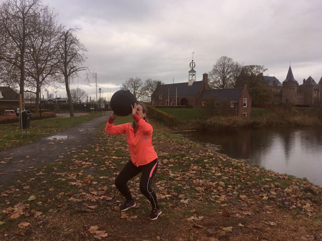 Training met een medicineball langs het water bij kale bomen